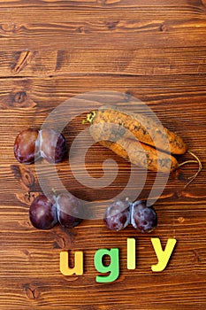 Plums and carrot on wooden background. Trendy ugly food concept. Fruit with a strange shape. The problem of food waste