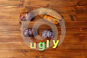 Plums and carrot on wooden background. Trendy ugly food concept. Fruit with a strange shape. The problem of food waste