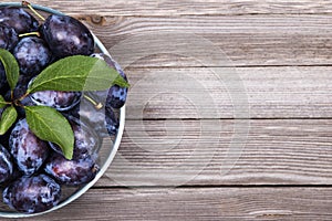 Plums with green leaves in a bowl on wooden background. Top view.