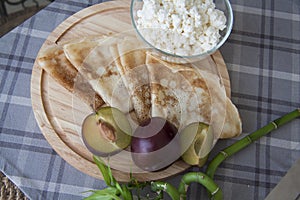 Plums and pancakes on wooden plate