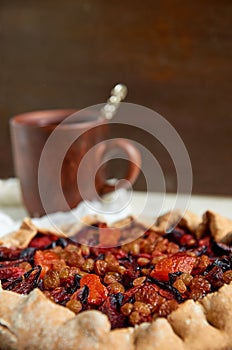 Plums pie with dried apricots close up. On blurred background a cup of tea on brown wooden background