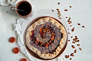 Plums pie with dried apricots on dark plate decorated with brown raisins and a cup of tea on light table with white cloth