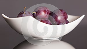 Plums on plate on grey background.