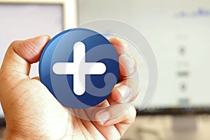 Plus icon blue round button holding by hand infront of workspace background