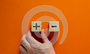 Plus or minus. Businessman holds a cubes with plus icon. Wooden cube with minus icon. Beautiful orange background. Copy space.