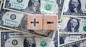 Plus or minus. Wooden cubes with plus and minus icon. Beautiful background from dollar bills. Copy space. Business and plus and