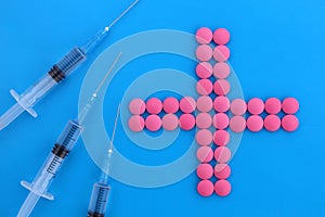 A plus sign is laid out from the pills, three syringes lie nearby.