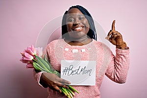 Plus size african american woman holding best mom message and tulips on mothers day surprised with an idea or question pointing