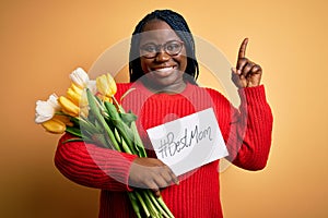 Plus size african american woman holding best mom message and tulips on mothers day surprised with an idea or question pointing