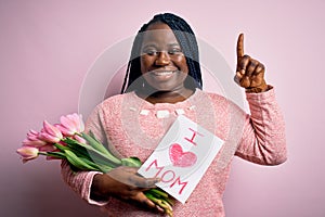 Plus size african american woman holding love mom message and tulips on mothers day surprised with an idea or question pointing