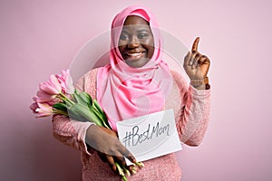 Plus size african american woman wearing hijab holding message and tulips on mothers day surprised with an idea or question