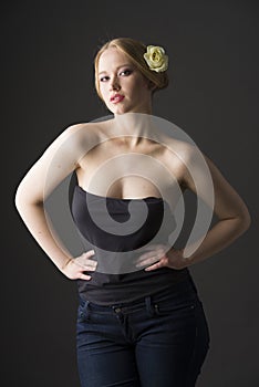 Plus size blonde with a yellow rose in her hair posing on a gray seamless background