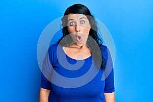 Plus size brunette woman wearing casual blue shirt afraid and shocked with surprise expression, fear and excited face