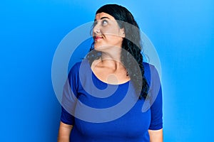 Plus size brunette woman wearing casual blue shirt smiling looking to the side and staring away thinking