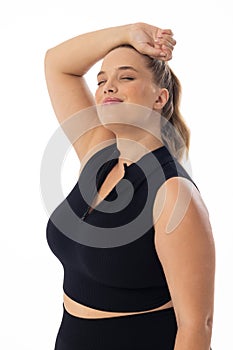 Plus size Caucasian female model stretches arm behind head on white background