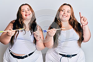 Plus size caucasian sisters woman eating eel sushi using chopsticks surprised with an idea or question pointing finger with happy