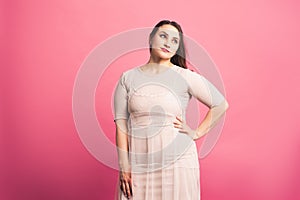 Plus size fashion model in beige dress, fat woman on pink background