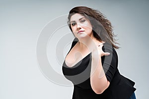 Plus size fashion model in black dress, fat woman on gray background, body positive concept