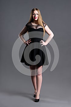 Plus size fashion model in black dress, fat woman on gray studio background, overweight female body