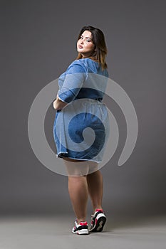 Plus size fashion model in casual jeans clothes, fat woman on gray background, overweight female body