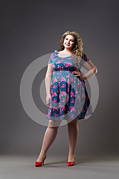 Plus size fashion model in floral dress, fat woman on gray background