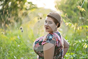 Plus size fashion model in floral dress outdoors, beautiful fat woman with big breasts in nature