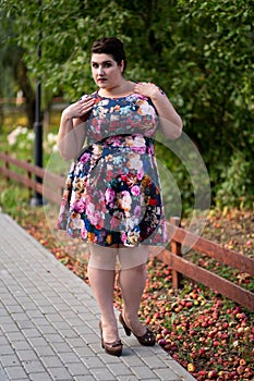 Plus size fashion model in floral dress outdoors, beautiful fat woman with big breasts in nature