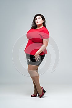 Plus size fashion model in red blouse and black skirt, fat woman on gray background, body positive concept