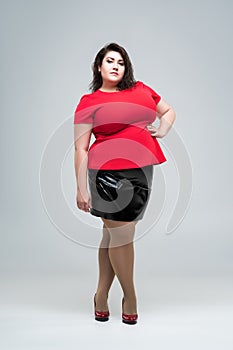 Plus size fashion model in red blouse and black skirt, fat woman on gray background, body positive concept