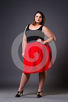 Plus size fashion model in red skirt, fat woman on gray background, overweight female body photo