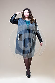 Plus size fashion model salutes in casual clothes, fat woman on beige studio background, overweight female body