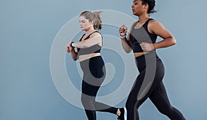 Plus size female checking her smartwatch while jogging outdoors with her friend