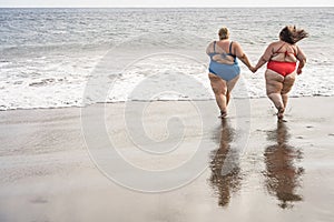 Plus size friends walking together on the beach having fun during summer vacation - Focus on women back