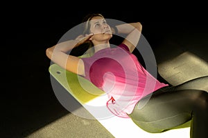 Plus size girl pump press in fitness gym on mat, black shadow background. Sweating woman do cardio workout by lifting