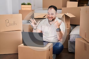 Plus size hispanic man with beard moving to a new home doing video call pointing thumb up to the side smiling happy with open