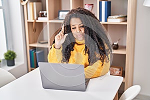 Plus size hispanic woman using laptop at home smiling with an idea or question pointing finger with happy face, number one