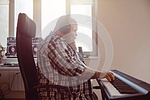 Plus size man with beard and headphones composes music on synthesizer in well equipped studio photo