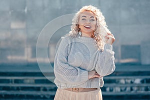 Plus size model with blond curly hair in knitted sweater outdoor