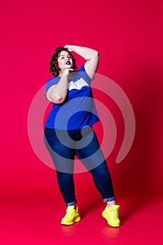 Plus size model in casual clothes, fat woman in blue jeans and t-shirt on red background