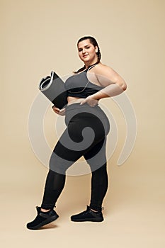 Plus Size Model. Fat Woman In Black Sportswear Full-Length Portrait. Smiling Brunette Holding Fitness Mat.