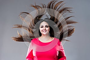 Plus size model with long hair blowing in the wind, brunette fat woman on gray background, body positive concept