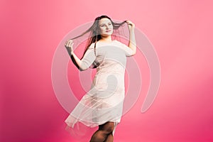 Plus size model with long hair blowing in the wind, fat woman on pink background