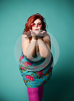 Plus-size overweight redhead lady in fashion sunglasses send a kiss on mint photo