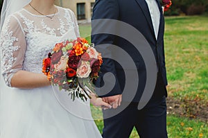 Plus size wedding couple is walking outside. Curvy bride is holding beautiful colorful bouquet with orange, red and pink peonies