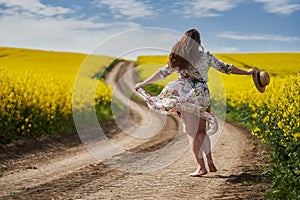 Plus size woman in floral dress, barefoot, on a road between canola fields