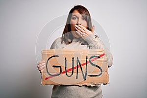 Plus size woman holding stop guns cardboard banner warning about violence cover mouth with hand shocked with shame for mistake,
