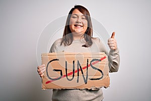 Plus size woman holding stop guns cardboard banner warning about violence happy with big smile doing ok sign, thumb up with