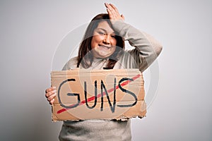 Plus size woman holding stop guns cardboard banner warning about violence stressed with hand on head, shocked with shame and