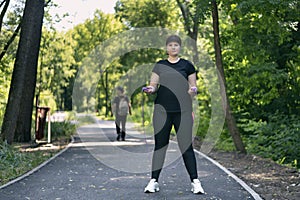Plus size woman jumping rope in the park and looks at the camera. Young woman in activewear choosing healthy lifestyle. Body