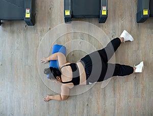 A plus-size woman lies on a gym floor, resting or unmotivated, surrounded by exercise equipment